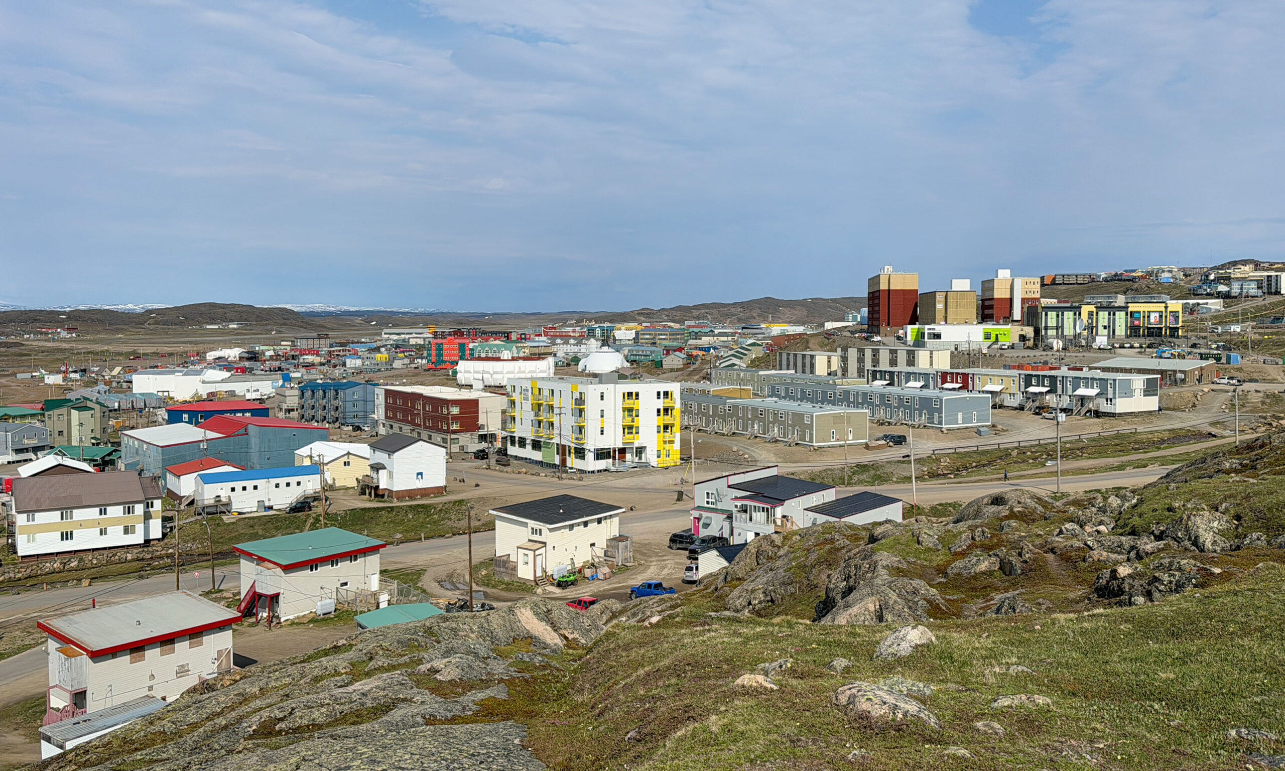 Skyline of Iqaluit, Nunavut, with low-rise buildings along the shoreline and hills in the background.